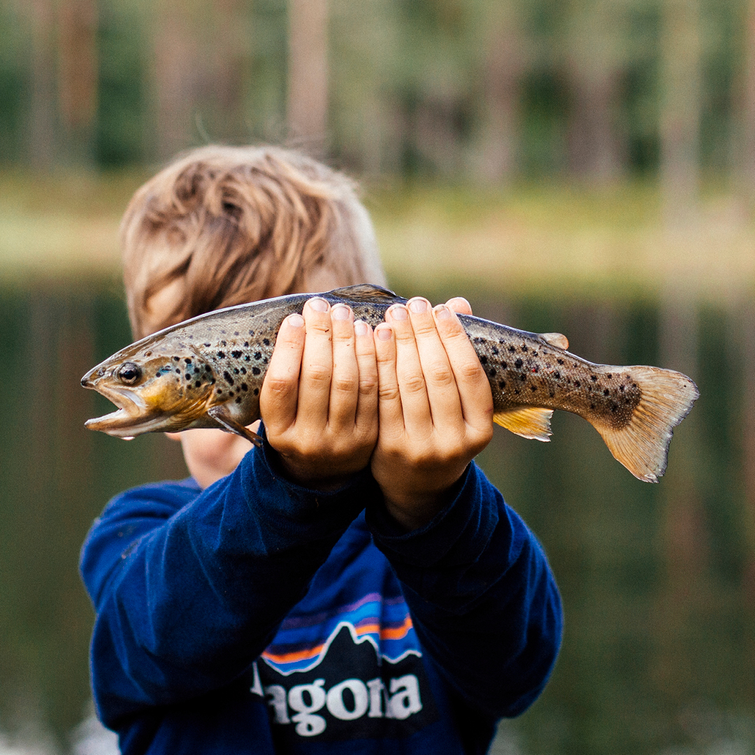Gutt i Patagonia genser som holder opp en fisk
